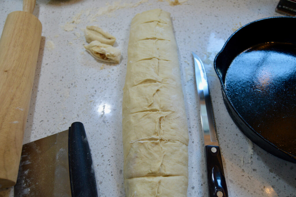 Cutting pear butter sourdough cinnamon rolls to be placed in the pan.