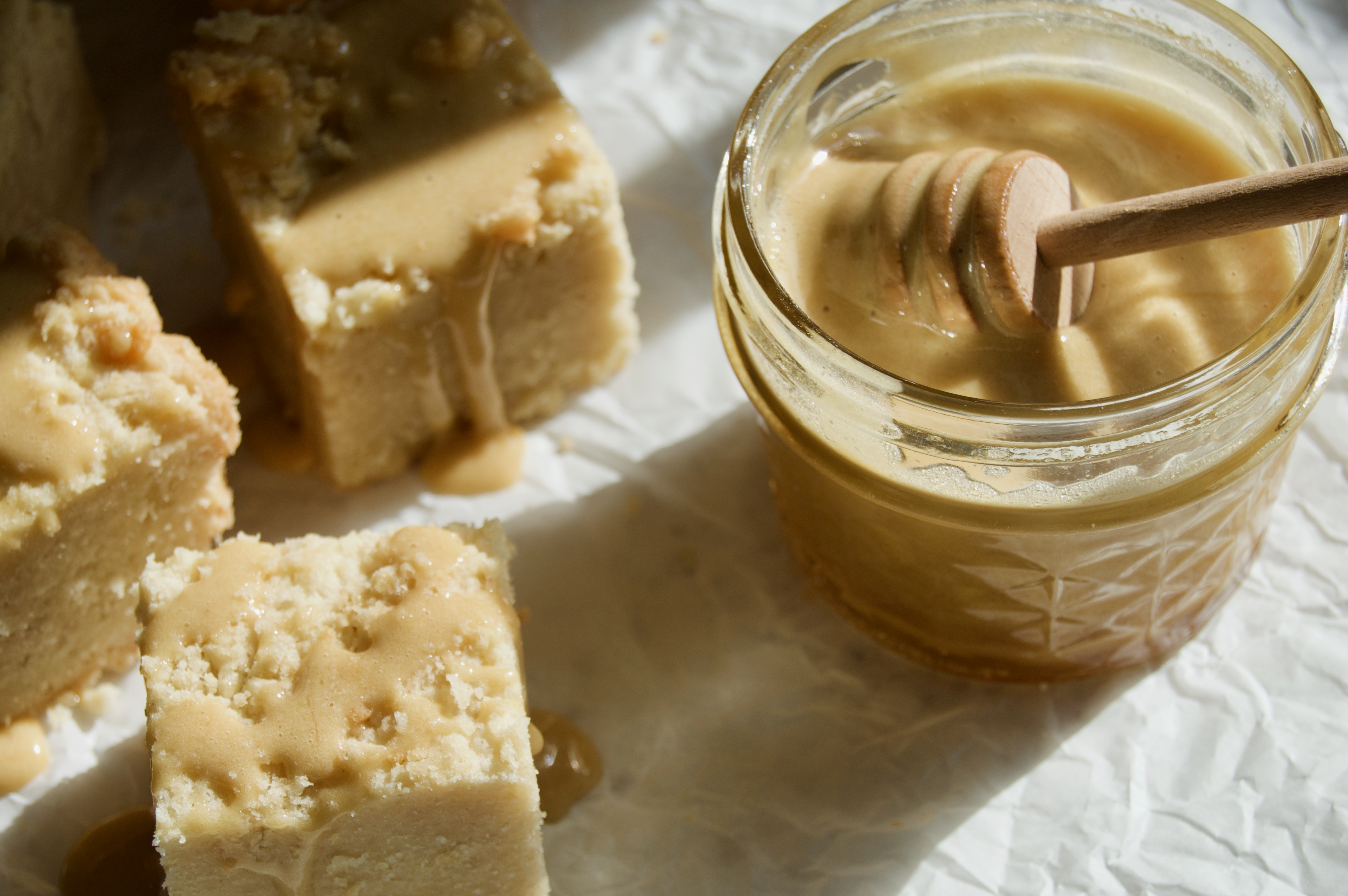 Natural light on creamy honey in glass jar that is drizzled on shortbread bars