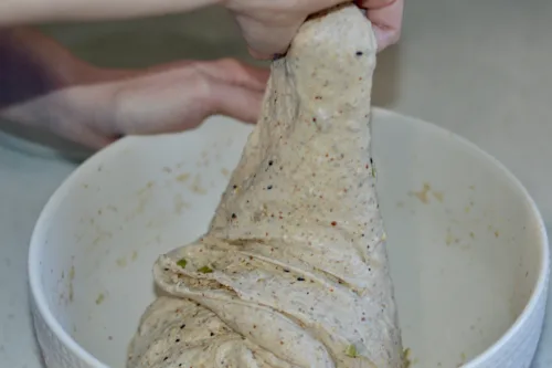 hands stretching corner of dough in large bowl
